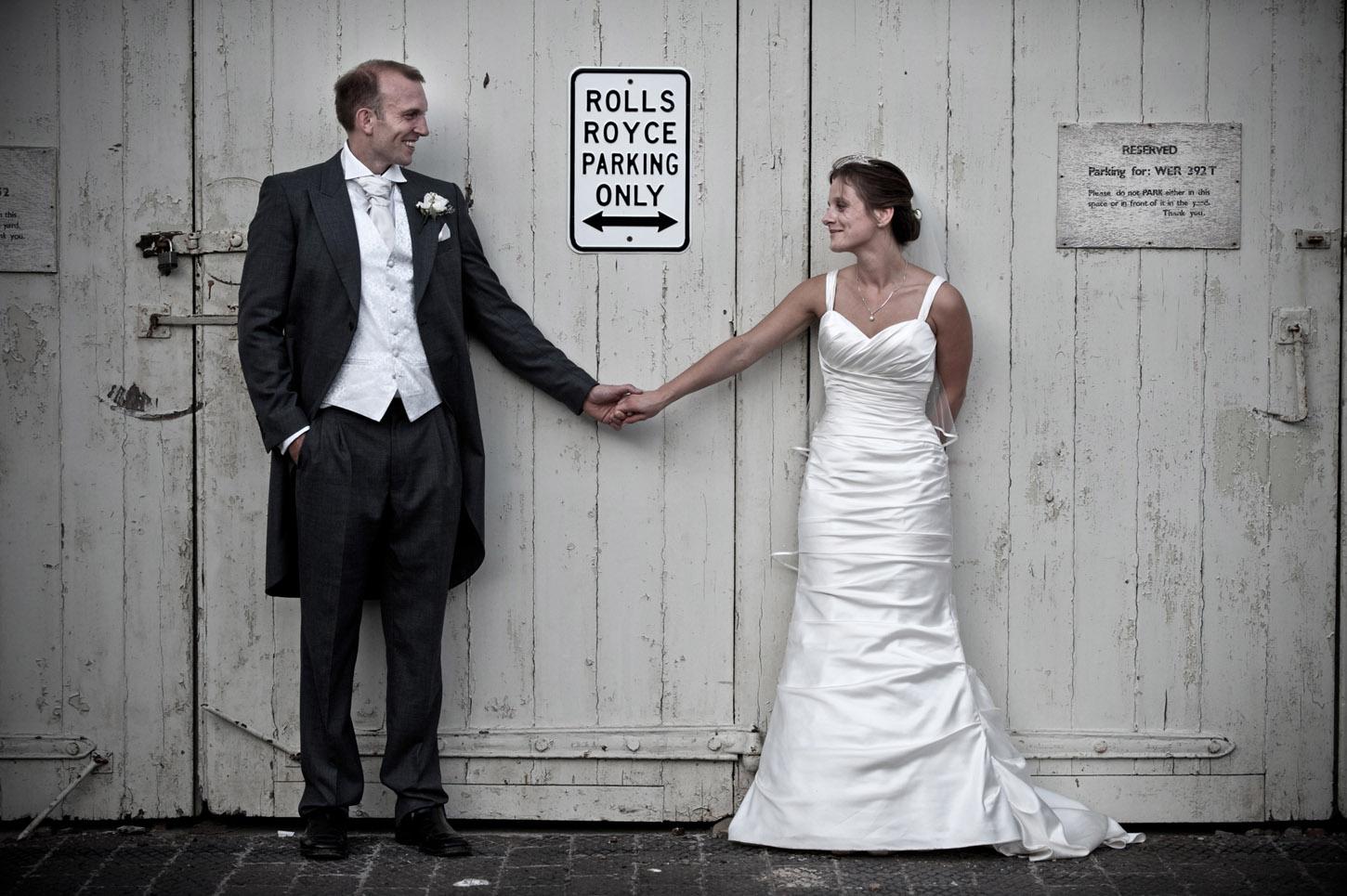 Bride and groom holding hands in front of a Rolls Royce Parking Only sign, UK wedding photography by MadlyWed