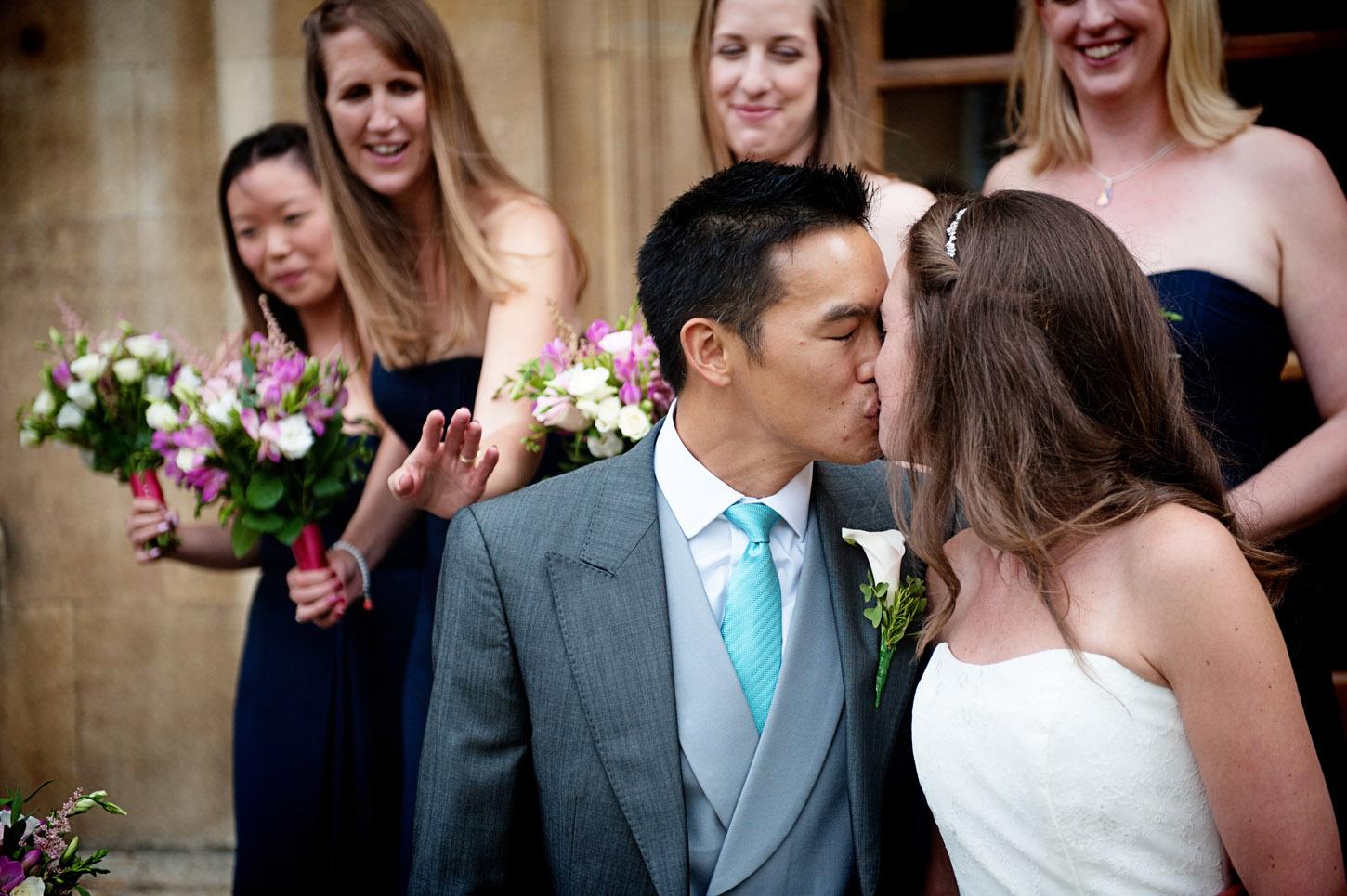 Groom kissing bride after the ceremony with bridesmaids smiling behind, UK wedding photography